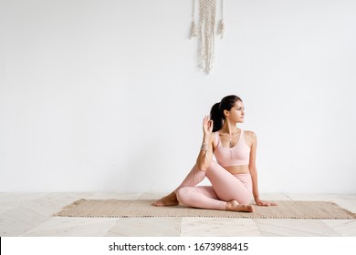 Positive caucasian young brunette woman doing Half lord of the fishes exercise, Ardha Matsyendrasana pose doing yoga. Yoga teacher woman doing gomukhasana on white background. Advertising space
