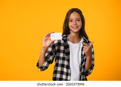 Positive caucasian young girl teenager kid schoolchild pointing showing credit card for shopping online, debt loan payments, e-banking isolated in yellow background.