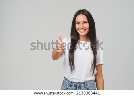 Positive caucasian young girl woman in white T-shirt showing thumb up looking at camera, checking for good quality recommendation isolated in grey background. Well done! Great job!
