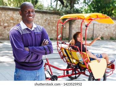Positive cheerful African-American man recommending traveling through city with pedicab