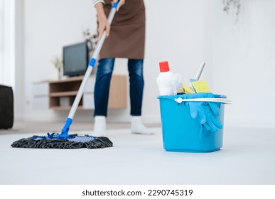 Positive cheerful girl having mop washing floor wearing brown apron fell content enjoy household chores in living room house indoors.Pretty young lady wiping floor with mop,  free space.