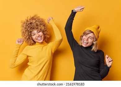 Positive, fröhliche junge Frauen haben Spaß und tanzen sorgenfreie Schüttelarme gekleidet in Gelegenheitsengpässen haben frohe Ausdrücke einzeln auf gelbem Hintergrund. Das Konzept des Glücks und der Gefühle der Menschen