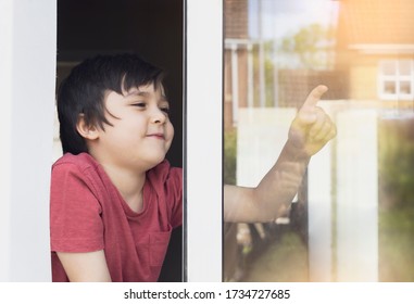 Positive Child Boy Sitting At The Window Writing On Glass And  With Smiling Face, School Kid In Self Isolation Relaxing At Home During Qualrantine Covid 19, Home Schooling , Distance Education