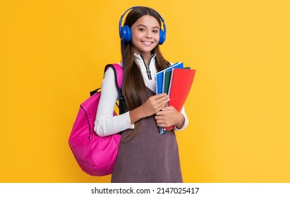 Positive Child In Headphones With School Backpack With Workbook On Yellow Background