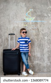 Positive Child Wearing Sunglasses Planning Her Vacation. Sketches Plans Trip Sea Around Concrete Wall Background Drawn Son With Chalk Free Space. Family Holiday Dreams Prepare Suitcase, Wait Departure