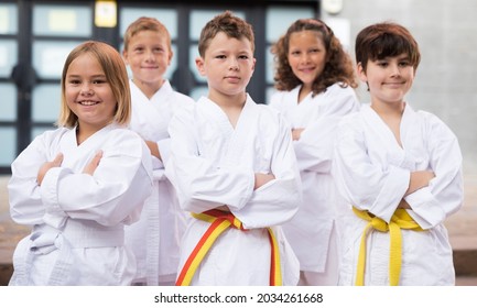 Positive children wearing white sports uniform practicing karate on a street near school