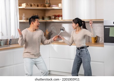 Positive Chinese Couple Having Fun While Cooking Together At Kitchen, Happy Asian Young Woman And Middle-aged Man Holding Kitchen Utensils, Fighting As Knights And Laughing, Side View