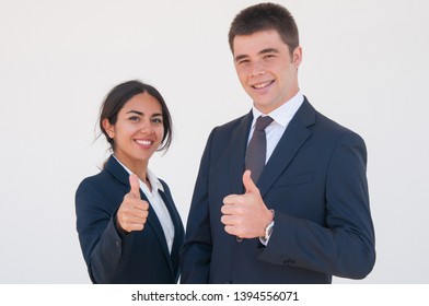 Positive confident business colleagues showing thumbs up. Young man and woman in formal jackets smiling at camera and expressing approval. Successful career concept