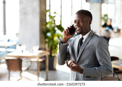 Positive Confident Young Black Manager With Beard Standing In Lobby Of Business Center And Gesturing Hand While Talking On Mobile Phone Cheerfully