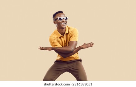 Positive cool dark-skinned man rejoices, has fun and dances isolated on background of mocha color. Funny african american man in casual clothes and sunglasses dancing waving his arms and laughing. - Powered by Shutterstock