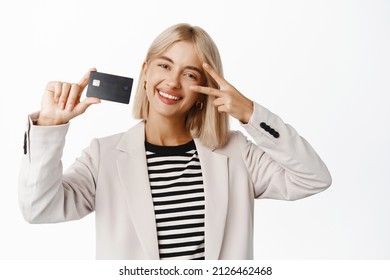 Positive corporate woman in suit, showing peace v-sign and credit card, demonstrating bank offer, standing over white background