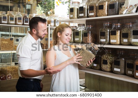 Positive couple having jar with dried herbs in hands in shop with ecological goods