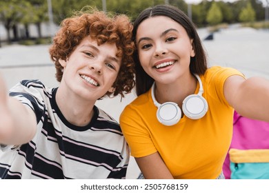 Positive couple of teenagers friends classmates students school pupils taking picture of themselves for selfie with smart mobile phone sitting spend time together in skate park ramp after lessons - Powered by Shutterstock