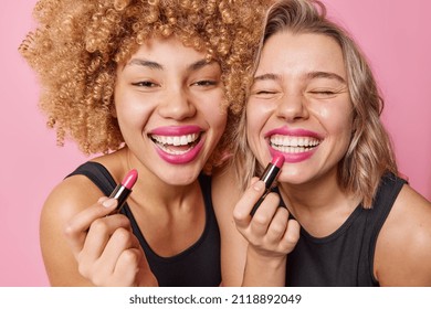 Positive curly two female models put on lipstick prepare for date or party smile toothily stand shoulder to shoulder have happy expressions pose indoor. Women cosmetics and beauty procedures - Powered by Shutterstock