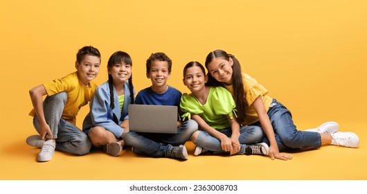 Positive cute multiracial preteen children sitting on floor and using laptop together isolated on yellow background. Diverse kids boys and girls studying online, playing video game, watching stream - Powered by Shutterstock