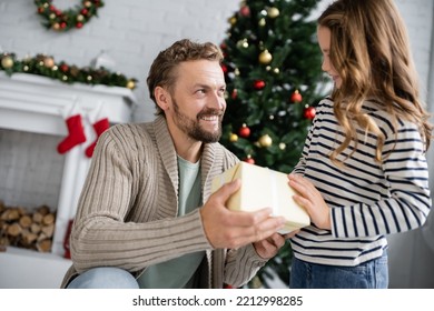 Positive Dad In Knitted Cardigan Giving Present To Daughter During Christmas At Home