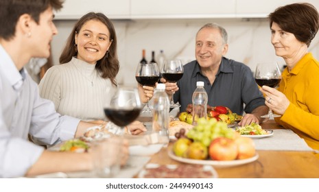 Positive daughter with boy-friend or husband and parents friendly conversation at dinner table with wine and light snacks in cozy kitchen - Powered by Shutterstock