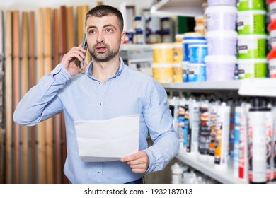 Positive Designer Is Choosing Paint With List For Redecorate House And Talking By Phone In The Store.