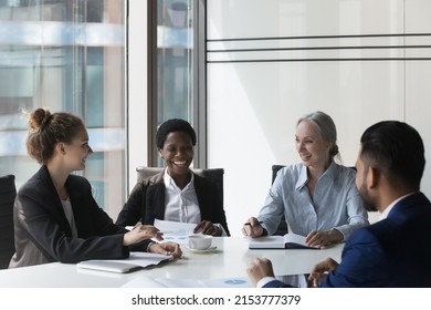 Positive diverse business team of different aged employees satisfied with financial reports, work result, talking at meeting table, laughing, enjoying teamwork, brainstorming, sharing creative ideas
