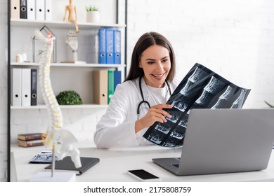 Positive Doctor Showing Mri Scan During Video Call On Laptop In Clinic