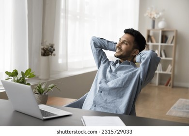 Positive dreamy Indian employee man thinking over career success, enjoying leisure, relaxation, work break at workplace, resting in office armchair, looking away, smiling, breathing fresh air - Powered by Shutterstock