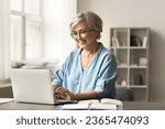 Positive elder mature freelance business lady enjoying online distant job from home, typing on laptop computer, smiling, working on freelance project, studying on Internet