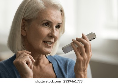 Positive elder senior lady talking on speaker on mobile phone, making call, holding smartphone at face, recording voice message, enjoying modern Internet communication. Close up casual portrait - Powered by Shutterstock