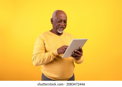 Positive elderly black man using digital tablet for freelancing job or studies on orange studio background. Happy senior African American teacher giving webinar online, speaking to students remotely - Powered by Shutterstock