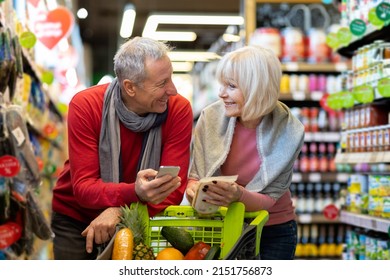 Positive elderly couple husband and wife shopping together at supermarket, standing at aisle with trolley, choosing products, holding modern smartphone, ckecking shopping list on gadget, chatting - Powered by Shutterstock