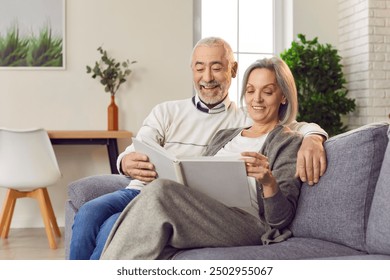 Positive elderly couple, wife and husband, is sitting on a sofa at home, looking at a family photo album. They are laughing together, reminiscing about happy memories captured in the photos. - Powered by Shutterstock