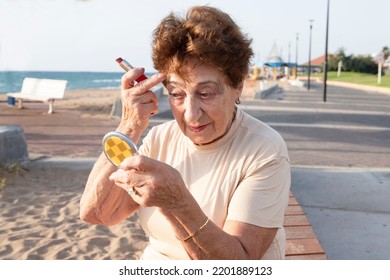 Positive Elderly Woman Fixing Makeup Looking In Small Mirror. Beautiful Woman Of 80 Years Old Sits Near The Sea. Concept Of Active Life Style, Retirement Time, Healthy, Happy Old Age, Skin. Caucasian.