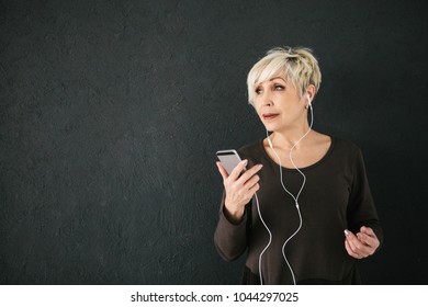 Positive elderly woman listening to music. On a dark background. The older generation and new technologies.