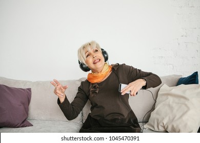 A positive elderly woman listens to music and sings. The older generation and new technologies.