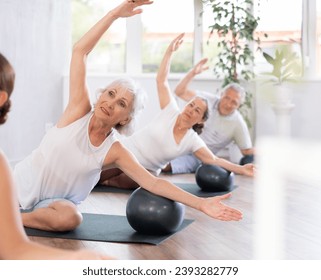 Positive elderly woman posing with soft ball at group class in modern yoga studio - Powered by Shutterstock