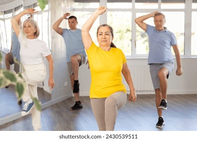 Positive elderly woman practicing Tai Chi with group of aged people, promoting health and wellness in bright training room - Powered by Shutterstock