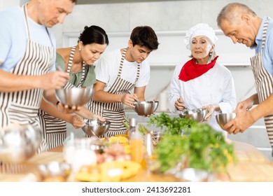 Positive elderly woman professional chef conducting culinary courses, imparting cooking skills to diverse group of people of different ages.. - Powered by Shutterstock