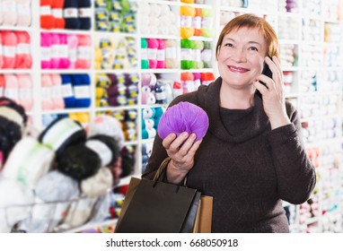 Positive elderly woman with shopping bags using phone in needlework store - Powered by Shutterstock