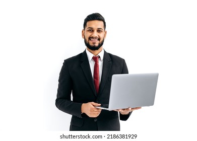 Positive Elegant Attractive Indian Or Arabian Man In Business Suit, Entrepreneur, Holding Open Laptop In Hands, Looks At Camera, Standing Over Isolated White Background, Smiles Friendly. Copy-space