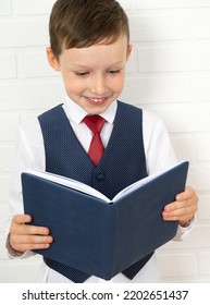 Positive Elementary School Nerd Student Holding An Open Textbook And Looking Into A Book On A Light Background