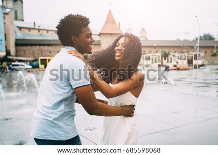 Positive emotional photo of amazing young african american couple whirling and hugging over city square with fountain on background. Travel recreation lifestyle, water fountain.
