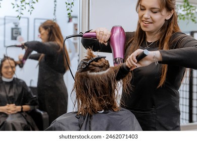  Positive, emotional woman professional hairdresser doing hair styling to client in beauty salon, stylist doing hair care procedures, drying hair with hairdryer to client - Powered by Shutterstock