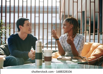 Positive emotional young businesswoman discussing news and ideas with colleague at meeting