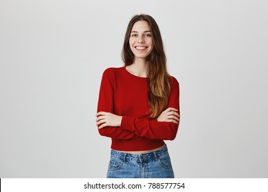 Positive emotions, good vibes. Portrait of young cute female student with long dark hair in casual hip outfit smiling, crossing hands, having photo session for graduation album
