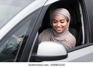 Positive emotions, happy driver goes to office in city, covid-19 pandemic. Smiling young pretty arabian muslim african american female in hijab watching rearview mirror sitting in new car, copy space