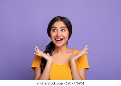 Positive Emotions. Portrait of excited indian woman spreading hands isolated over purple studio background. Sale And Discount Concept. Emotional young female model looking aside at free space