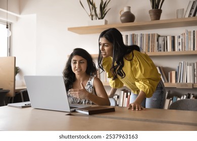 Positive engaged young Indian female business colleagues talking at laptop, discussing online work project, Internet content, teamwork strategy. Professional consulting coworker at workplace - Powered by Shutterstock