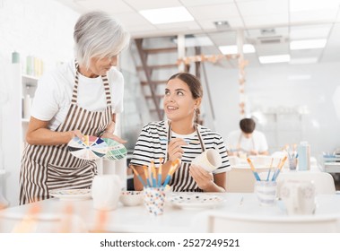 Positive enthusiastic senior woman offering guidance to interested young girl painting ceramic mug in pottery class. Creative hobby concept.. - Powered by Shutterstock