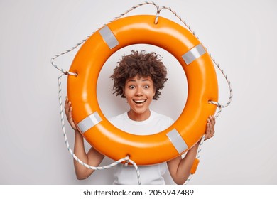 Positive Ethnic Female Looks Through Lifesaver Smiles Broadly Ready For Summer Vacations Dressed In Casual T Shirt Isolated Over White Background. Glad Afro American Woman Learns To Swim With Lifebuoy