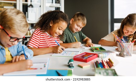 Positive Ethnic Student Girl Smiling And Writing Down Data Into Notebook While Sitting At Table Near Classmates During Test At School