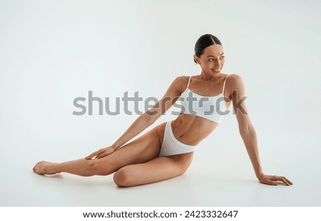 Positive facial expression. Woman in white underwear with slim body type against white background.
